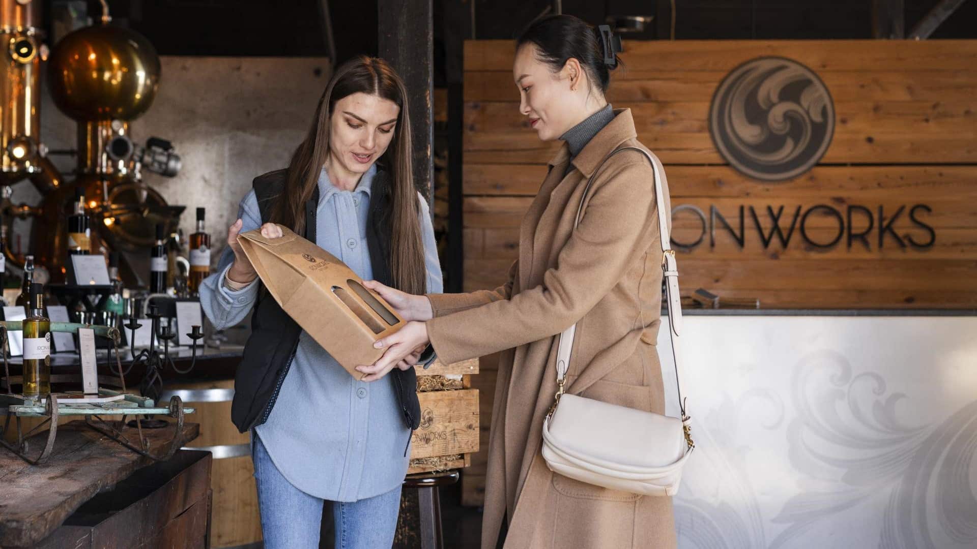 Two women are shopping and looking at a brown carton of boxed spirits