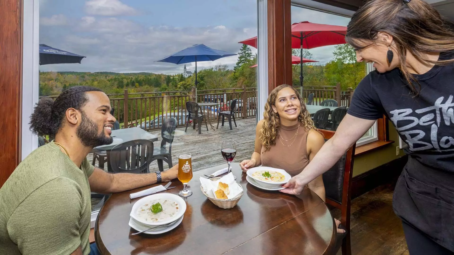 Two people dining at Henley House restaurant in Sheet Harbour, Nova Scotia with a server placing a meal in front of one of them