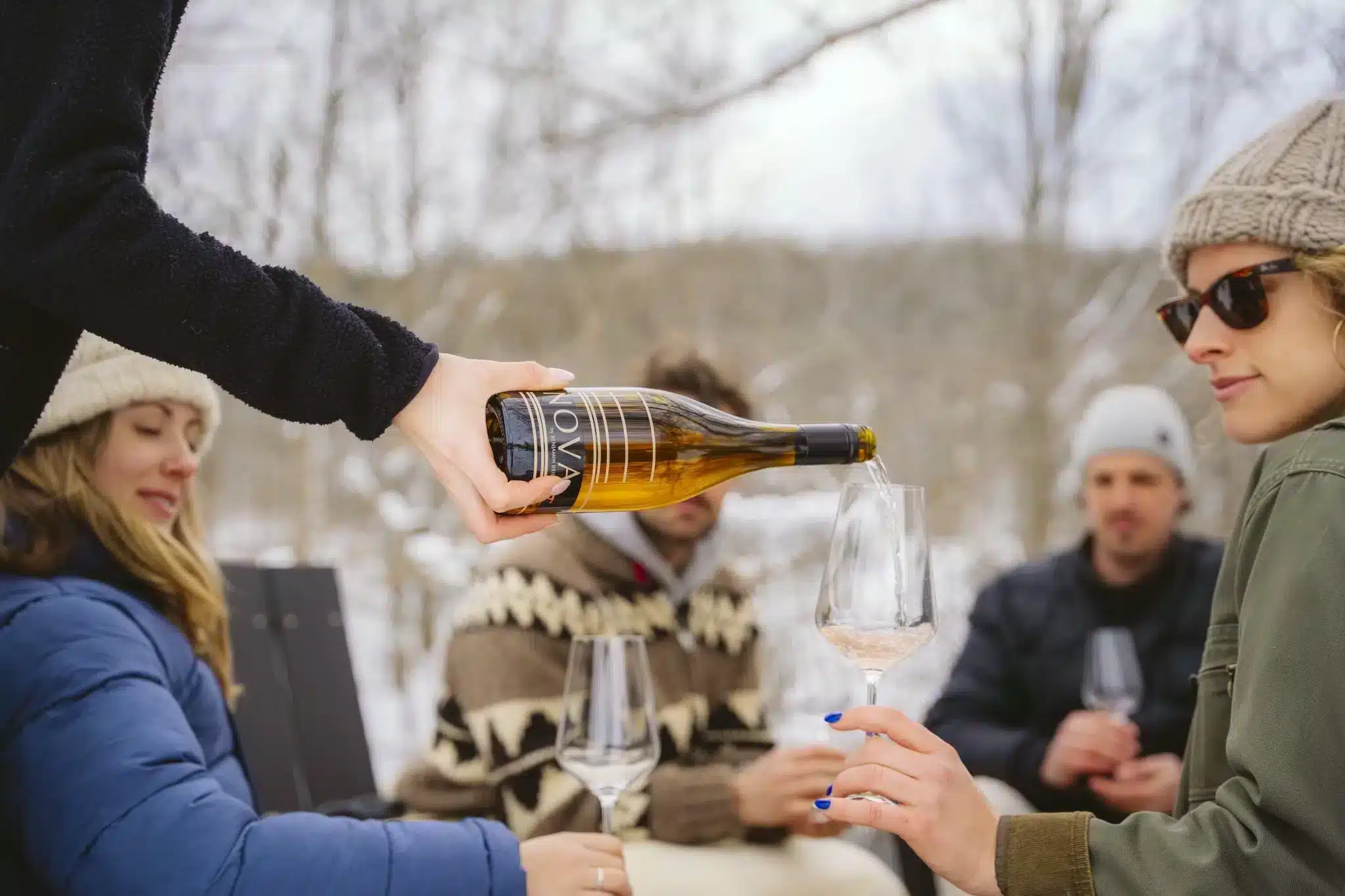 Guests, seated in chairs outdoors in the winter time, being poured wine at Benjamin Bridge Vineyards.